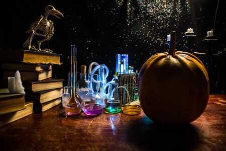 Wizard's Desk. Horror Halloween concept. Magic potions in bottles on wooden table with books and candles. Halloween still-life background with different elements on dark toned foggy background. Selective focusの写真素材
