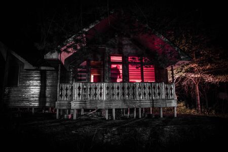Old house with a Ghost in the forest at night. Horror silhouette at the window. Old building in forest. Surreal lights. Horror Halloween conceptの写真素材