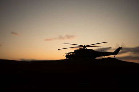Silhouette of military helicopter ready to fly from conflict zone. Decorated night footage with helicopter starting in desert with foggy toned backlit. Selective focus. War conceptの写真素材