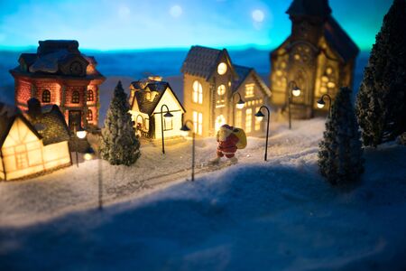 Little decorative cute small houses in snow at night in winter, Christmas and New Year miniature house in the snow at night with fir tree. Holiday concept. Selective focusの写真素材