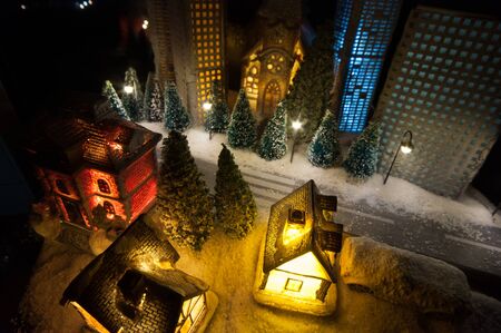 Little decorative cute small houses in snow at night in winter, Christmas and New Year miniature house in the snow at night with fir tree. Holiday concept. Selective focusの写真素材