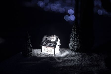 Little decorative cute small houses in snow at night in winter, Christmas and New Year miniature house in the snow at night with fir tree. Holiday concept. Selective focusの写真素材