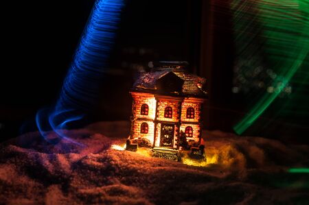 Little decorative cute small houses in snow at night in winter, Christmas and New Year miniature house in the snow at night with fir tree. Holiday concept. Selective focusの写真素材