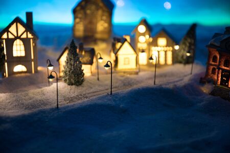 Little decorative cute small houses in snow at night in winter, Christmas and New Year miniature house in the snow at night with fir tree. Holiday concept. Selective focusの写真素材