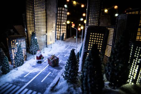 Little miniature city with road and lights. Decorative cute small houses in snow at night in winter. Creative Holiday concept. Christmas and New Year attributes decorated composition.の写真素材