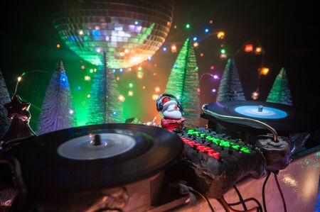 Christmas and New Year club concept. Dj mixer with headphones on snow. Santa Claus is mixing on turntable. Creative miniature artwork decoration on snow.の写真素材
