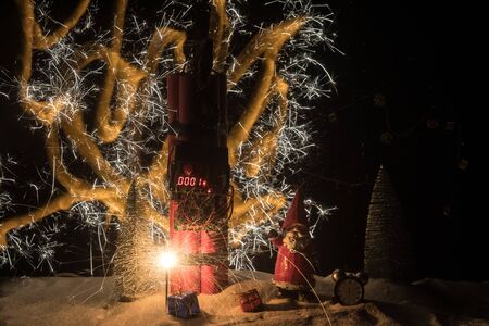 Christmas and New Year funny concept. Time bomb (dynamite) on snow with holiday decor and santa....