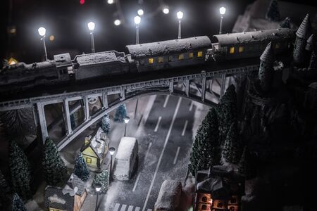 Miniature of winter snowy scene with train on bridge, medieval castle and small city. Holiday attributes. Night scene. New Year and Christmas concept. Creative artwork mini on table decorationの写真素材