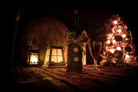 Glass of wine with Christmas decoration. Red wine in crystal glass with bottle on colorful carpet with creative New Year artwork decorations. Copy spaceの写真素材