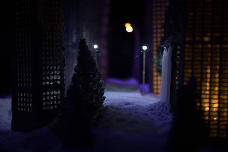 Little miniature city with road and lights. Decorative cute small houses in snow at night in winter....