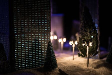 Little miniature city with road and lights. Decorative cute small houses in snow at night in winter. Creative Holiday concept. Christmas and New Year attributes decorated composition.の写真素材
