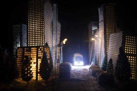 Little miniature city with road and lights. Decorative cute small houses in snow at night in winter. Creative Holiday concept. Christmas and New Year attributes decorated composition.の写真素材