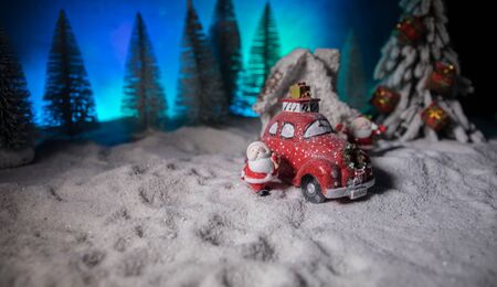 Christmas and New Year holidays concept. Little decorative cute small red car in snow at night. Traditional holiday attributes on snow. Creative artwork decorations. Empty space for your textの写真素材