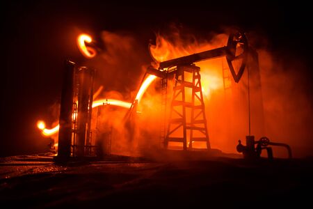 Oil pump and oil refining factory at night with fog and backlight. Energy industrial concept. Selective focus. Artwork decoration.の写真素材