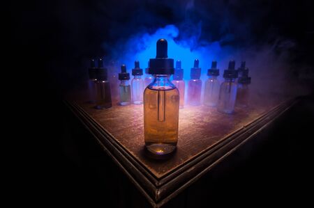 Vape concept. Smoke clouds and vape liquid bottles on dark background. Light effects. Useful as background or vape advertisement or vape background. Selective focusの写真素材