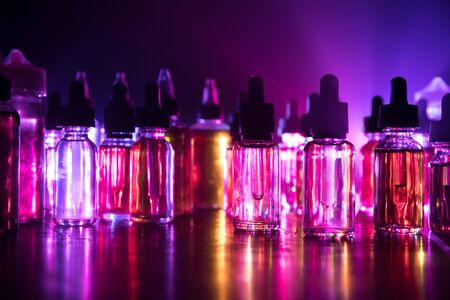 Vape concept. Smoke clouds and vape liquid bottles on dark background. Light effects. Useful as background or vape advertisement or vape background. Selective focusの写真素材