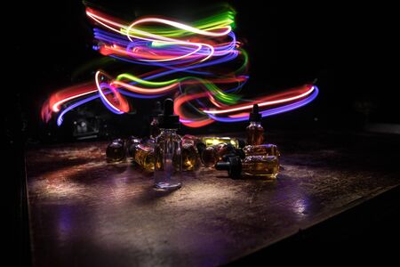 Vape concept. Smoke clouds and vape liquid bottles on dark background. Light effects. Useful as...