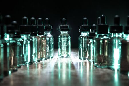 Vape concept. Smoke clouds and vape liquid bottles on dark background. Light effects. Useful as background or vape advertisement or vape background. Selective focusの写真素材