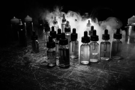 Vape concept. Smoke clouds and vape liquid bottles on dark background. Light effects. Useful as background or vape advertisement or vape background. Selective focusの写真素材