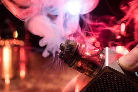 Vape concept. Electronic Cigarette vape explosion. Smoke clouds and vape liquid bottles on dark background. Light effects. Useful as vape advertisement. Selective focusの写真素材