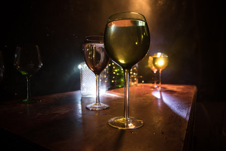 Goblet of wine on wooden table with beautiful toned lights on background. Glasses of wine on dark background. Selective focus. Club drink conceptの写真素材