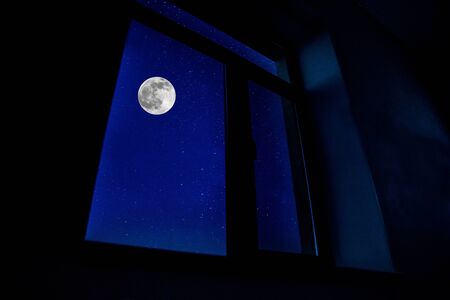Night scene of moon seen through the window from dark room. Moonlight inside dark roomの写真素材