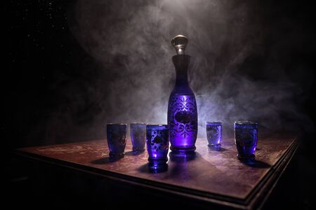 A beautiful blue carafe with vodka stands on a wooden table with glasses. Dramatic toned foggy...