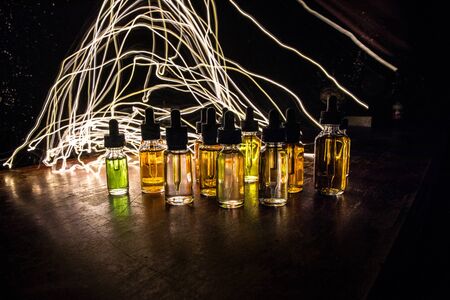 Vape concept. Smoke clouds and vape liquid bottles on dark background. Light effects. Useful as background or vape advertisement or vape background. Selective focusの写真素材