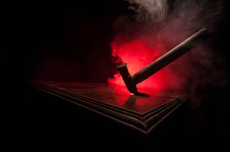 Old vintage hammer on a wooden table in front of a dark toned misty background. Selective focus.