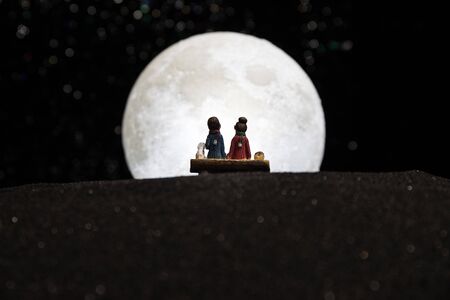 Silhouettes of a couple with starry and lunar background. Happy couple at night under moonlight. Creative artwork table decoration.の写真素材