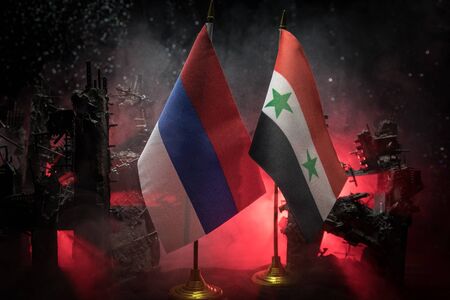 Closeup, flags of Russia and Syria against destroyed city at night. Decorated diorama. Concept of crisis of war and political conflicts between nations. Selective focusの写真素材