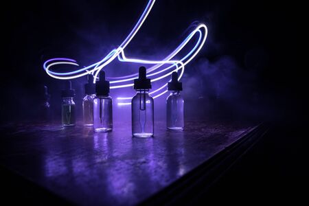 Vape concept. Smoke clouds and vape liquid bottles on dark background. Light effects. Useful as background or vape advertisement or vape background. Selective focusの写真素材