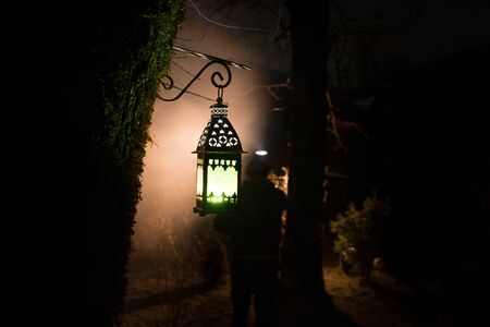 Beautiful colorful illuminated lamp in the garden in misty night. Retro style lantern at night outdoor. Selective focusの写真素材