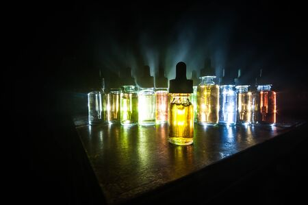 Vape concept. Smoke clouds and vape liquid bottles on dark background. Light effects. Useful as background or vape advertisement or vape background. Selective focusの写真素材