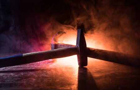 Old vintage hammer on a wooden table in front of a dark toned misty background. Selective focus.