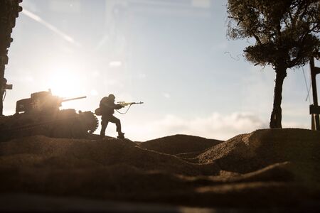 Army sniper with large caliber rifle standing in the fire and smoke. War Concept. Battle scene on war fog sky background, Fighting silhouettes Below Cloudy Skyline at sunset. City destroyed by warの写真素材