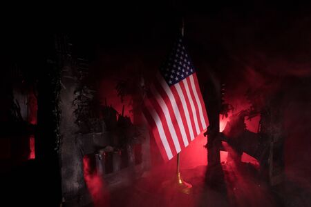 Closeup, flag of USA against destroyed city at night. Decorated diorama. Concept of crisis of war and political conflicts between nations. Selective focusの写真素材