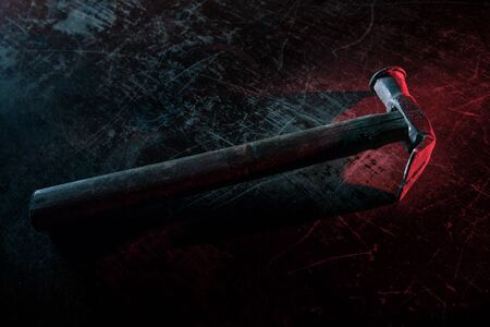 Old vintage hammer on a wooden table in front of a dark toned misty background. Selective focus.
