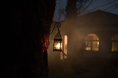 Beautiful colorful illuminated lamp in the garden in misty night. Retro style lantern at night...