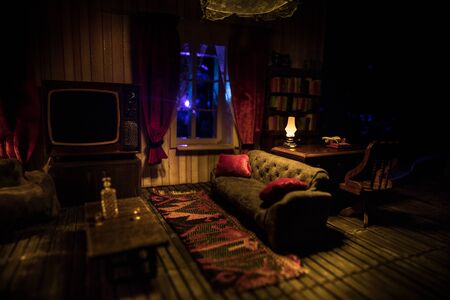 A realistic dollhouse living room with furniture and window at night. Artwork table decoration with handmade realistic dollhouse. Old retro style Television. Selective focus.の写真素材