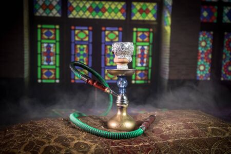 Hookah hot coals on shisha bowl making clouds of steam at Arabian interior. Oriental ornament on the...