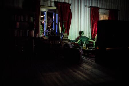 A realistic dollhouse living room with furniture and window at night. Artwork table decoration with handmade realistic dollhouse. Man wathing retro style Television in dark room. Selective focus.の写真素材
