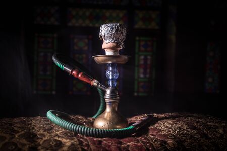 Hookah hot coals on shisha bowl making clouds of steam at Arabian interior. Oriental ornament on the carpet. Stylish oriental shisha in dark with backlight.の写真素材