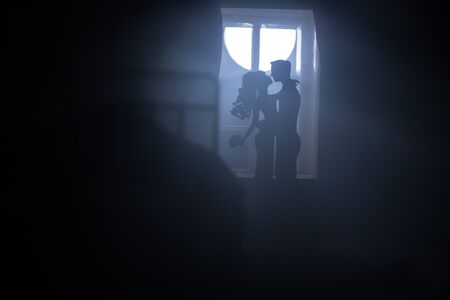 A realistic dollhouse bedroom with furniture and window at night. Romantic couple sitting on window. Man and woman making love in bedroom. Artwork table decoration . Selective focus.の写真素材