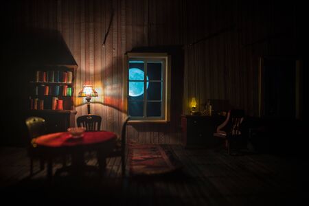 A realistic dollhouse living room with furniture and window at night. Man sitting on table in dark room. Concept of stay home during global virus pandemic. Selective focus.の写真素材