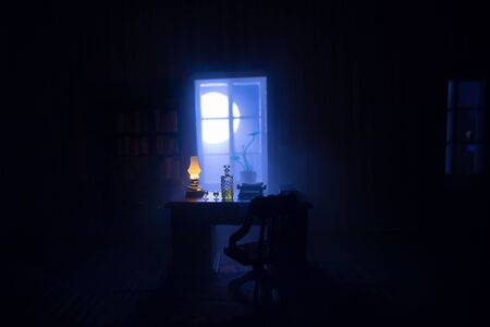 A realistic dollhouse living room with furniture and window at night. Man sitting on table in dark room. Concept of stay home during global virus pandemic. Selective focus.の写真素材