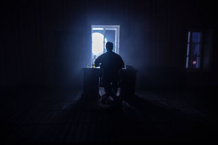 A realistic dollhouse living room with furniture and window at night. Man sitting on table in dark room. Concept of stay home during global virus pandemic. Selective focus.の写真素材