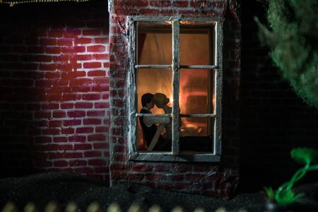 A realistic dollhouse living room with furniture and window at night. Romantic couple sitting on window. Artwork table decoration with handmade realistic dollhouse. Selective focus.の写真素材