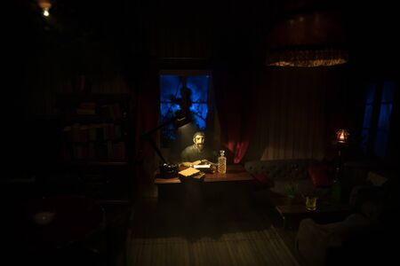 A realistic dollhouse living room with furniture and window at night. Man sitting on table in dark room. Selective focus.の写真素材