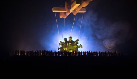 Creative concept of manipulation with coronavirus. Crowd looking on big Corona virus miniature. The hand controls the Covid19 miniature with strings on a dark foggy background. Selective focusの写真素材